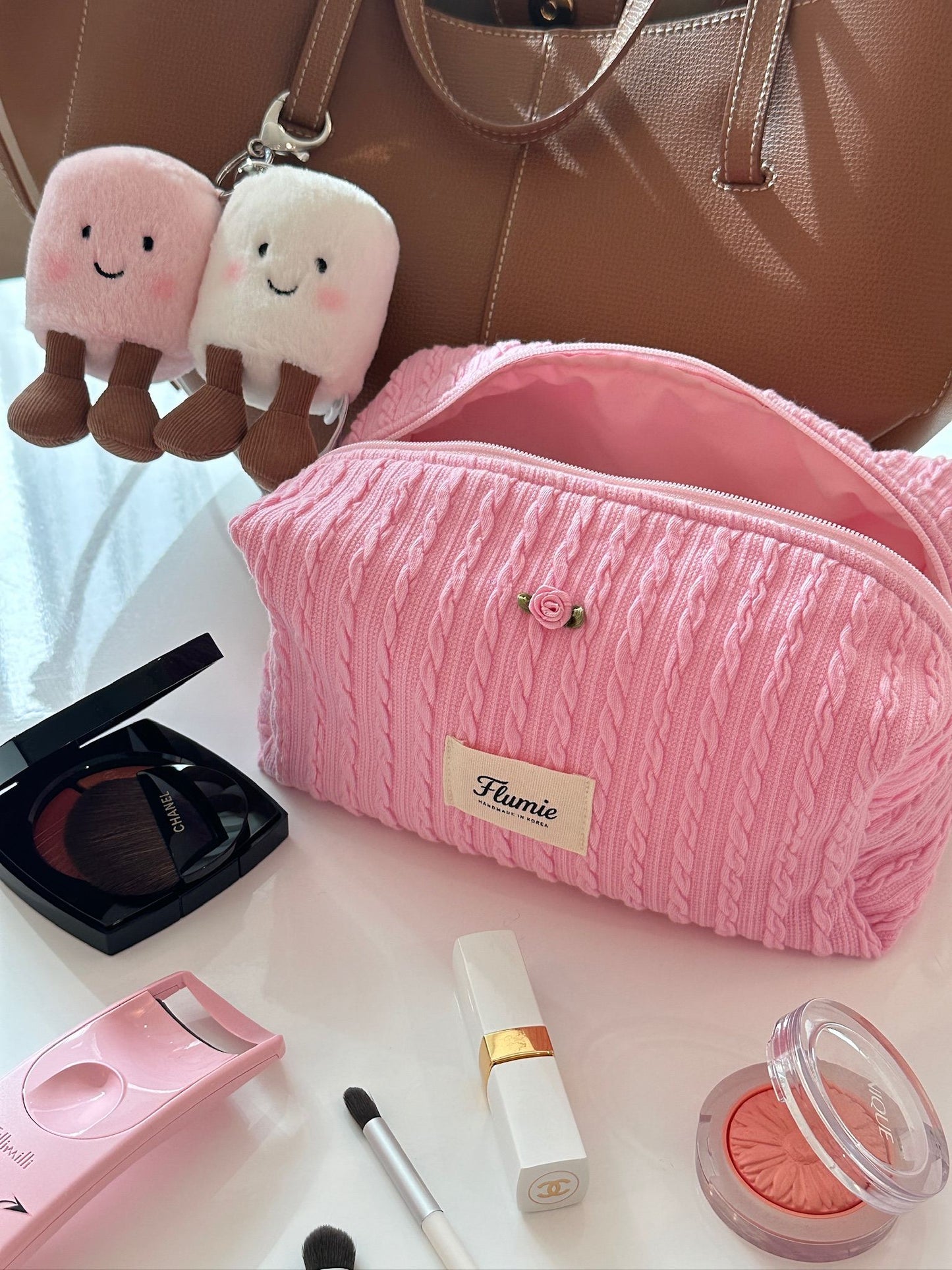 핑크 파우치와 립제품, 핸드미러가 함께 놓여 소녀스러운 데일리 뷰티 세트를 연출해요.